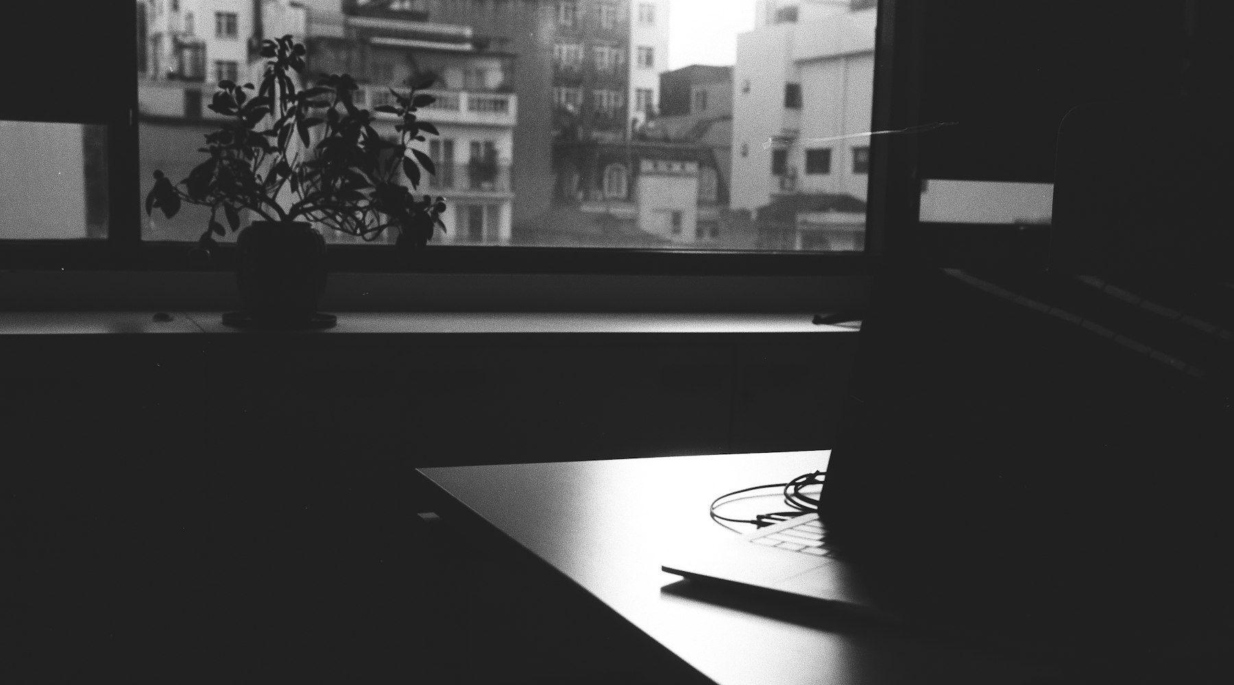 Monochrome workspace with desk, window light, and laptop
